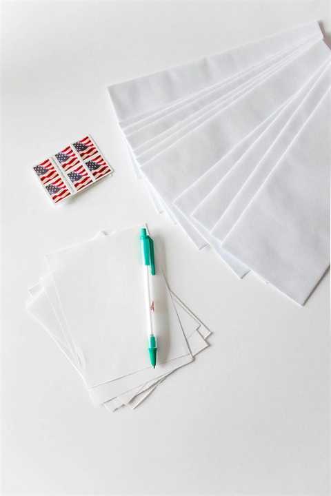 A white table displays a pen, several envelopes, and a colorful sticker arranged neatly.